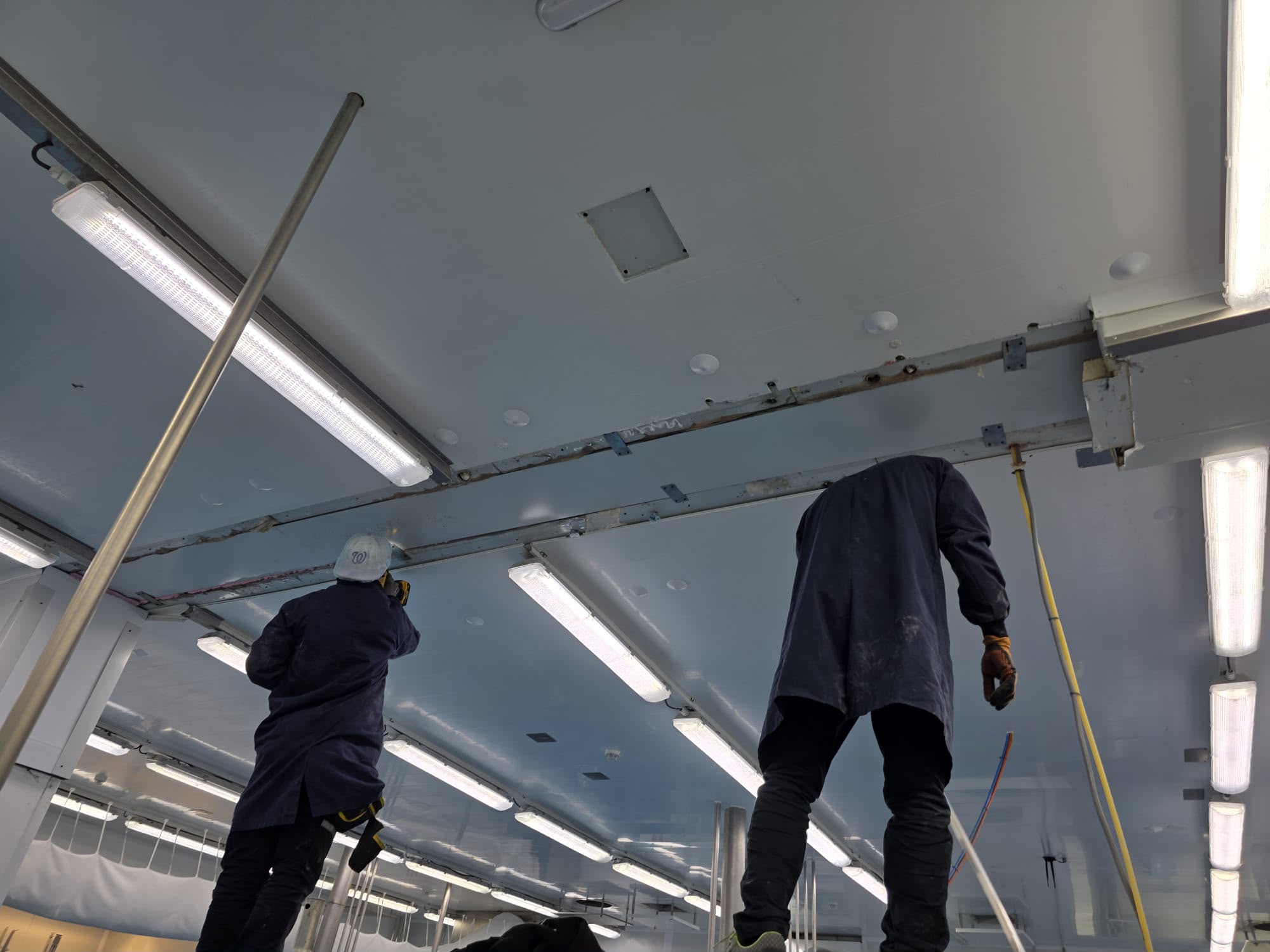 Dos operaris muntant sostre i lluminàries en una sala blanca